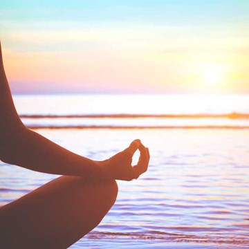 Mujer en pose de flor de loto frente a un atardecer en la playa